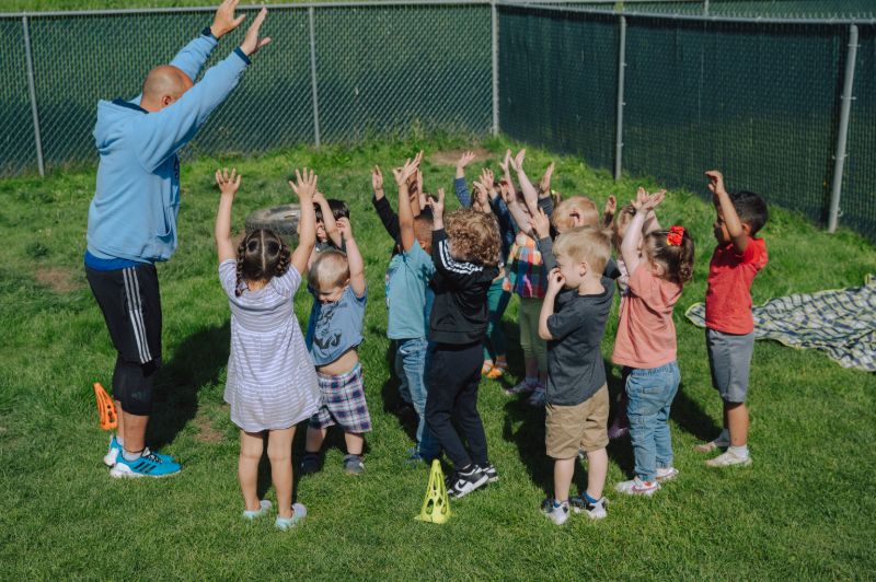 Preschool teacher leading outdoor play activity with children at Lil’ Patriots Academy Puyallup as part of the Abeka and HighScope blended curriculum.