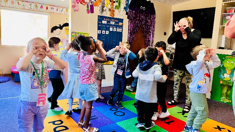 Children in a daycare classroom in Puyallup WA participating in a fun group activity led by a teacher, promoting learning and movement.