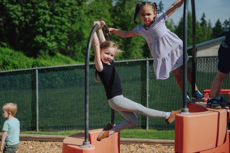 Two preschool girls enjoying outdoor climbing play at Lil’ Patriots Academy, part of the preschool program and kindergarten readiness in Puyallup.