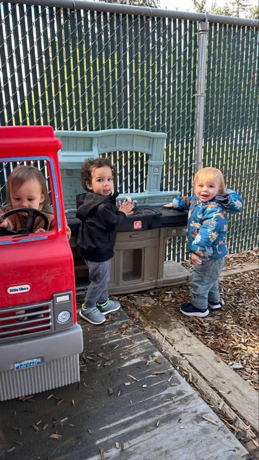 Young children enjoying outdoor play with a toy truck and activity station at a Spanaway childcare center.