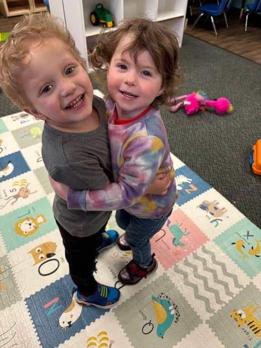 Two young children hugging and smiling together at a daycare in Spanaway WA that encourages social-emotional growth.