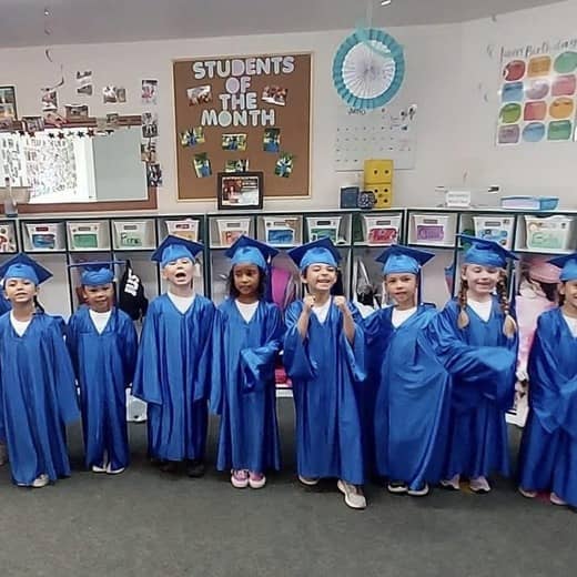 Children in blue caps and gowns during a preschool graduation ceremony at a Spanaway childcare center.